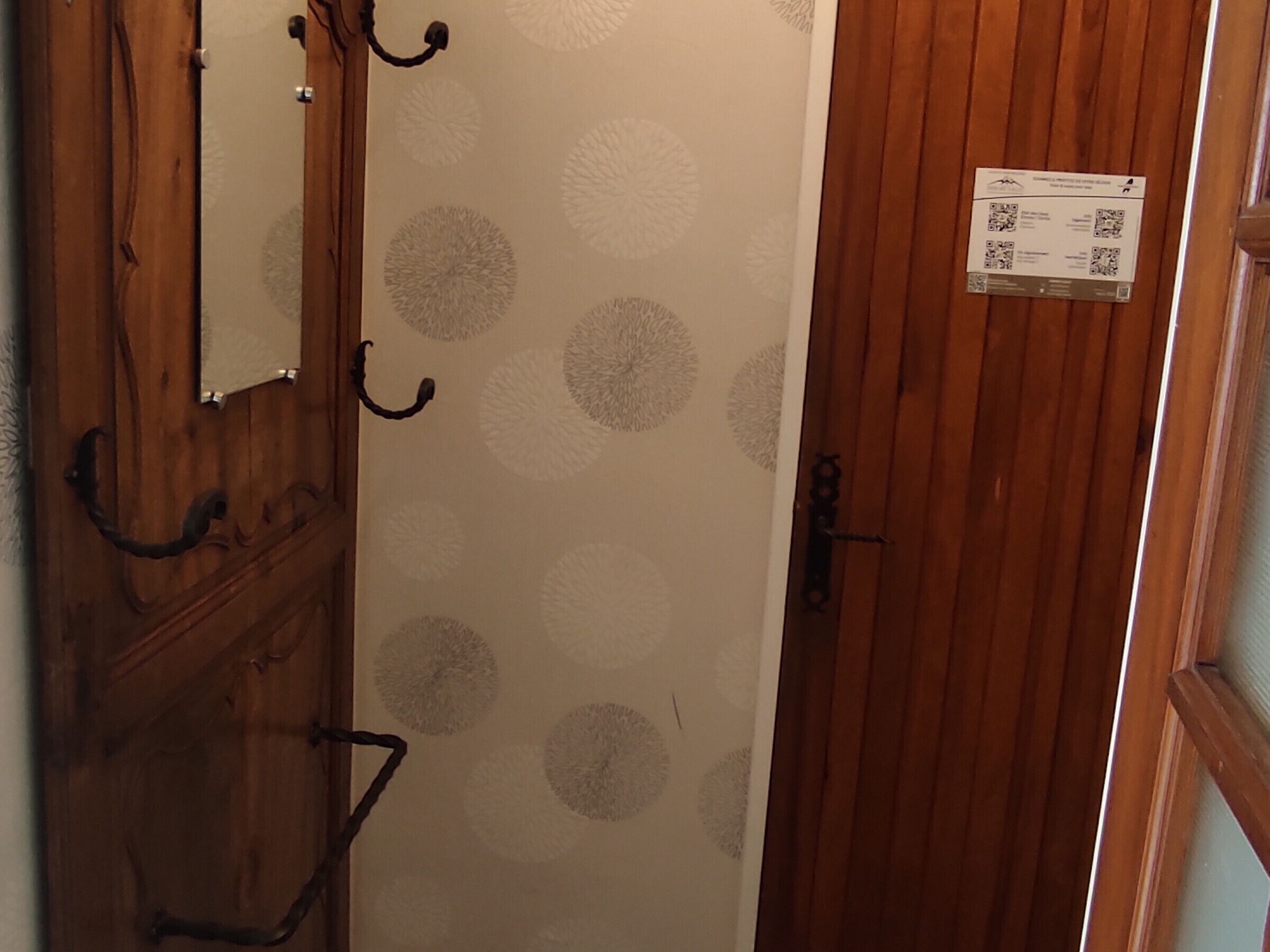 A wooden door with a circular pattern wallpaper, a metal handle, and a QR code sign.