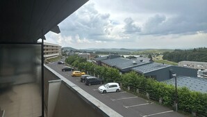 Ein Parkplatz mit mehreren Autos, ein Gebäude mit flachem Dach und eine Aussicht auf ferne Hügel unter einem bewölkten Himmel.