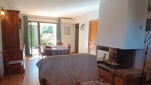 A cozy living room with a fireplace, a dining area with a table and chairs, and a covered sofa. - Air-conditioned villa with private pool and pets allowed (Saint-Génis-des-Fontaines)