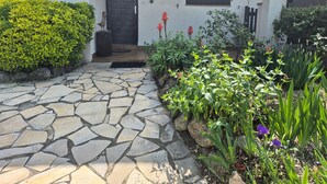 A stone-paved entrance with a door, a small porch, and various plants and flowers. - Air-conditioned villa with private pool and pets allowed (Saint-Génis-des-Fontaines)