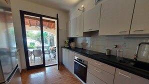 A compact kitchen with white cabinets, a black countertop, and a sliding glass door leading to an outdoor seating area. - Air-conditioned villa with private pool and pets allowed (Saint-Génis-des-Fontaines)