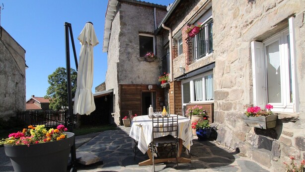 Un patio de piedra con una mesa preparada para comer, rodeado de plantas en macetas y mobiliario de exterior.