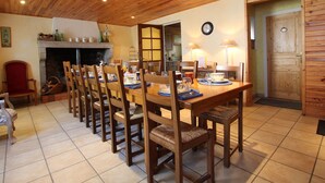 Un comedor con una mesa de madera dispuesta para cuatro personas, rodeada de sillas, una chimenea y una puerta de madera.