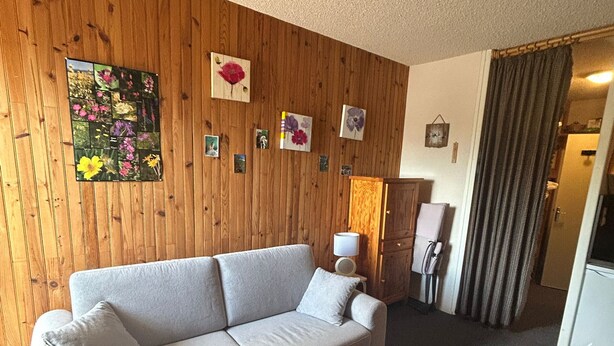 Ein Zimmer mit einem beigen Sofa, einer Holzwand mit gerahmten Bildern, einer Lampe und einer mit Vorhängen versehenen Tür.