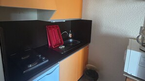 Eine kleine Küche mit schwarzer Arbeitsplatte, einem roten Abtropfgestell, einem Spülbecken und einem weißen Gerät.