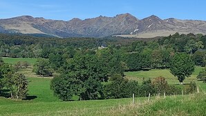 Eine gebirgige Landschaft mit einem kleinen Haus, umgeben von üppigem Grün und Bäumen.