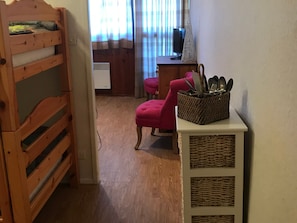A room with a bunk bed, a desk with a computer, a pink chair, and a wicker basket on a small table.