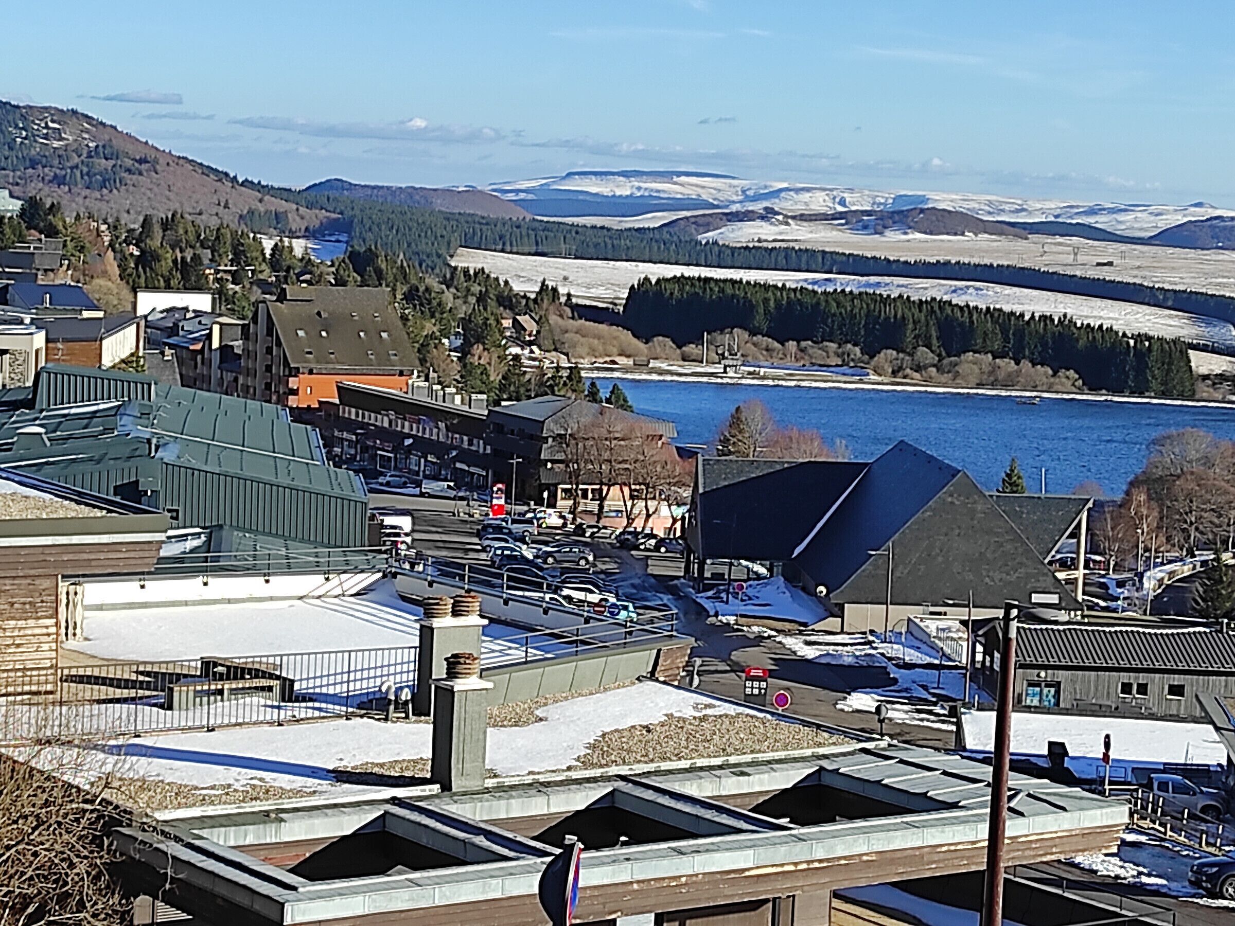 A town with buildings, a parking lot, and a body of water in the background.