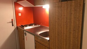 Cocina compacta con estufa, pileta y una pared de acento roja.