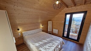 A wooden-paneled bedroom with a bed, bedside lamps, and a view through a glass door. - Modern chalet for 14 with private parking (Besse-et-Saint-Anastaise-Super Besse)