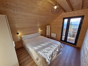 Un dormitorio con paneles de madera, una cama, lámparas de noche y vistas a través de un ventanal.