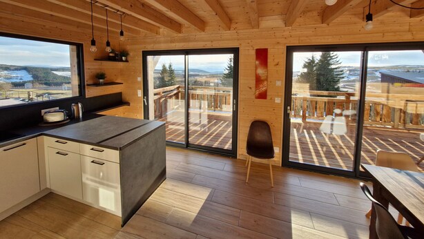 A modern kitchen with wooden beams, a large window, and a sliding glass door leading to an outdoor deck.