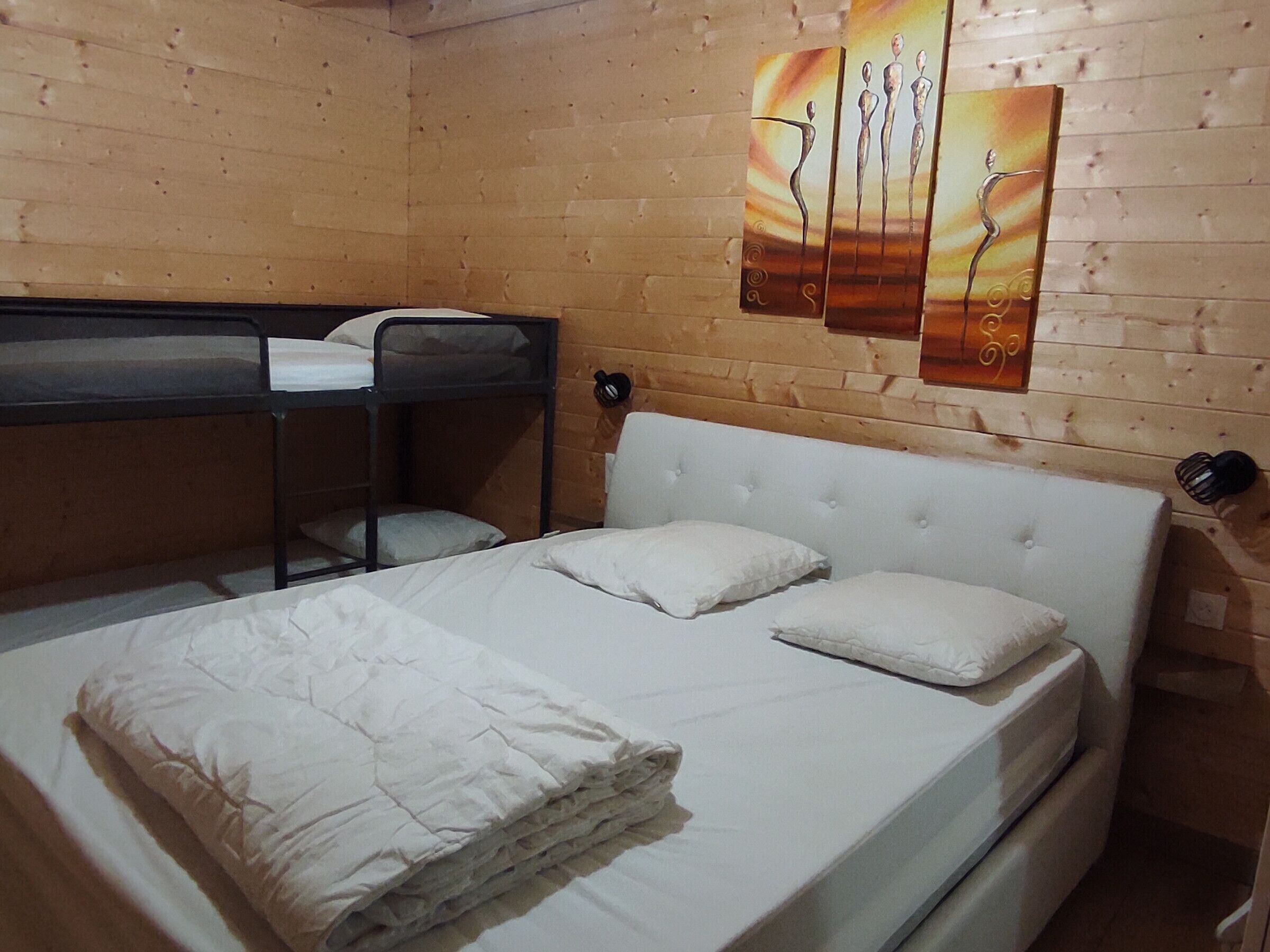 A bunk bed with a white headboard and pillows, a lower bunk with a mattress, and a wall-mounted shelf with a decorative item.