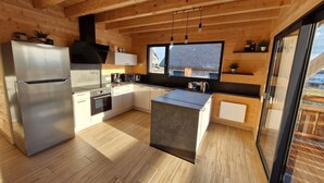 A modern kitchen with wooden beams, stainless steel appliances, and a large window offering a view of the outside.