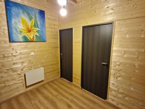 Una habitación con paneles de madera, dos puertas oscuras, un interruptor de luz y un cuadro de una flor.