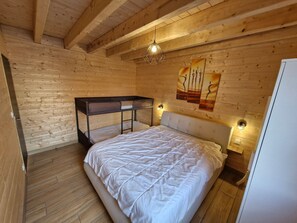 Ett rum med träpanel på väggarna, en våningssäng, en stor säng och två vägglampor.