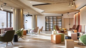Un área de descanso moderna con suelo de madera, diversas opciones de asiento, incluyendo sillas y otomanas coloridas, y una gran estantería.