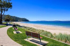 A beach with a paved walkway, benches, and a grassy area.