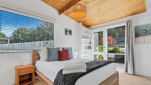 Un dormitorio con cama de madera, una mesita de noche, una ventana con persianas, una estantería y vistas al exterior.