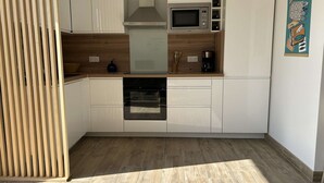 A modern kitchen with white cabinets, a built-in oven, a microwave, and a wooden countertop.