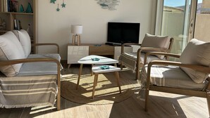 A cozy living room with a sofa, two armchairs, a small table, a TV, and a bookshelf.