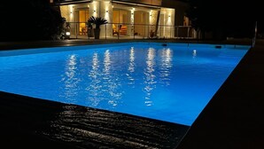 A modern two-story house with a swimming pool at night.