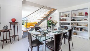 A modern dining area with a glass table, black chairs, and a staircase with wooden steps.
