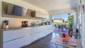 A modern kitchen with a built-in oven, a large window, and a dining area with a table and chairs.