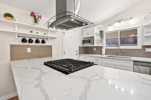 Eine moderne Küche mit Kochinsel, Edelstahlgeräten und einer Spritzschutzwand.