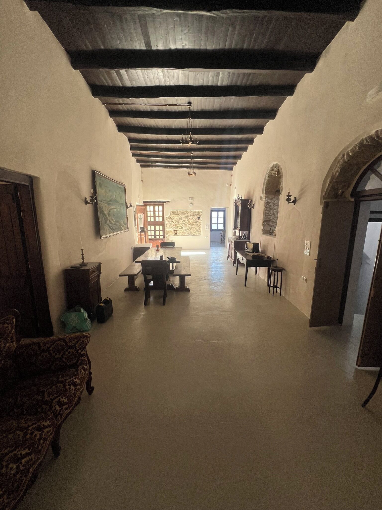 A spacious room with a high ceiling, wooden beams, and a central dining table with chairs.