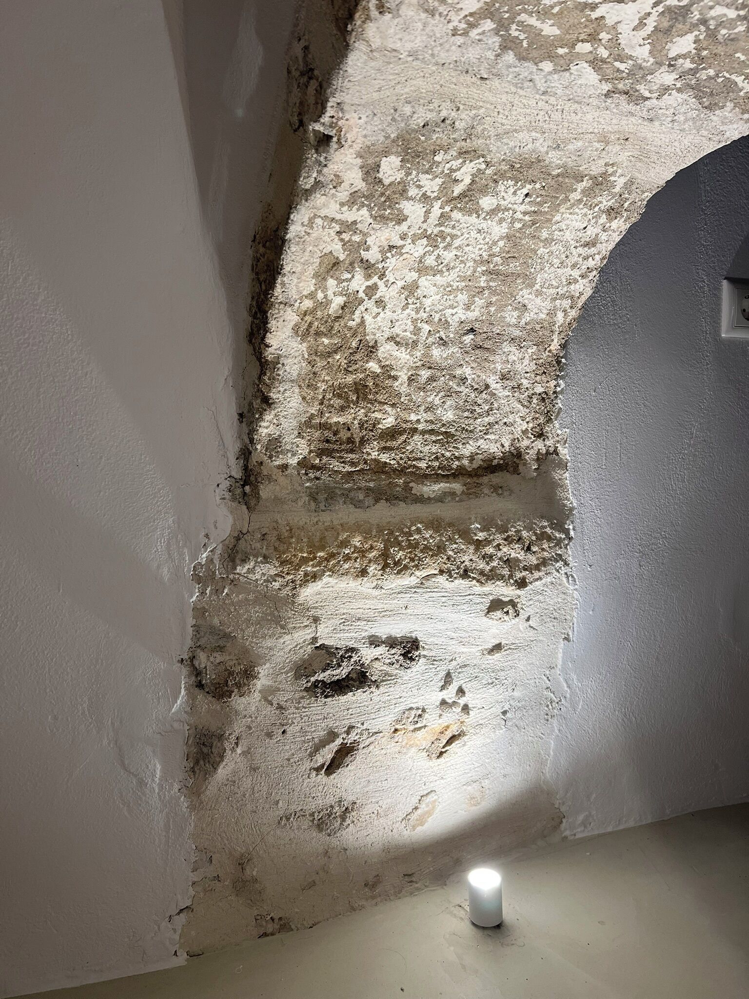 Quarto com parede texturizada, uma rachadura visível e uma pequena luminária no chão.