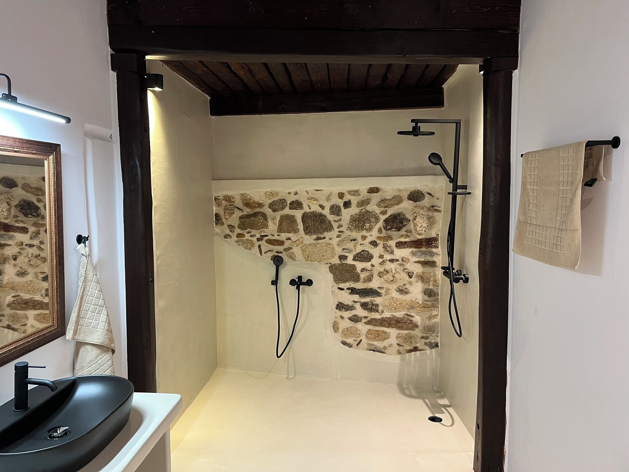 A bathroom with a stone shower wall, a black sink, and a towel hanging on a hook.