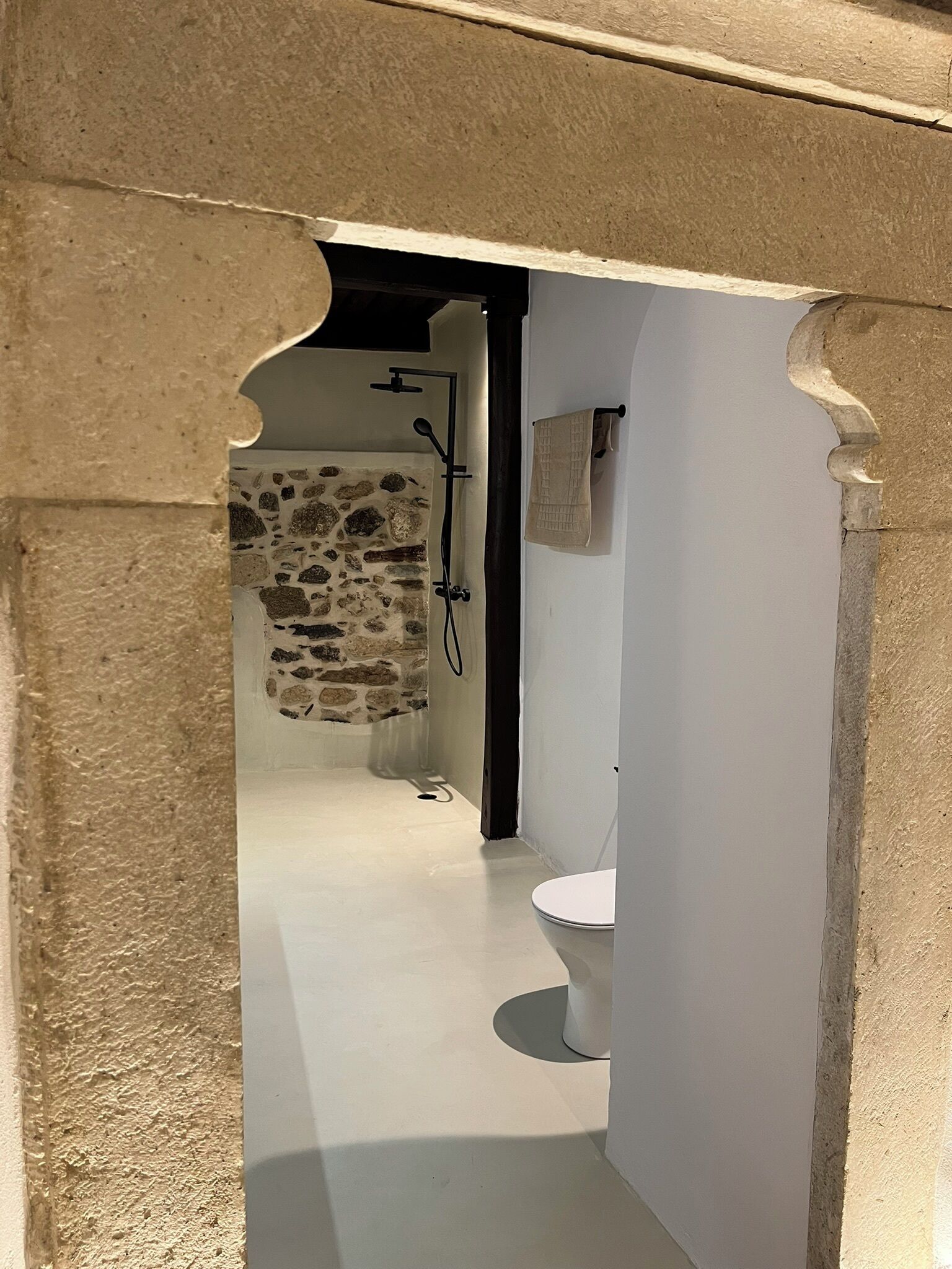 Een badkamer met een douchecabine van natuursteen, een wit toilet en een handdoekhouder.
