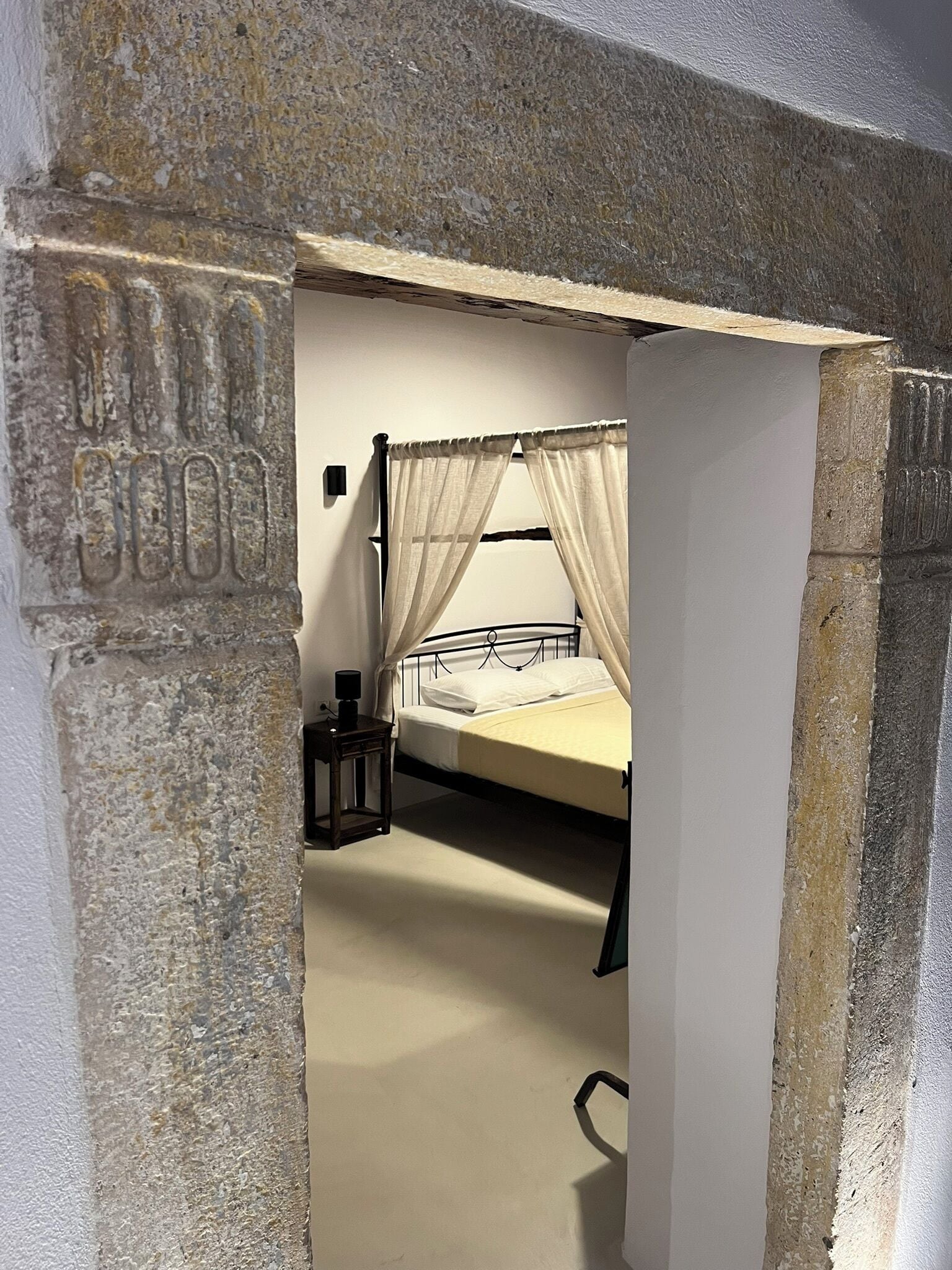 Ein Zimmer mit einem Bett, einem Nachttisch und einer Steinsäule.
