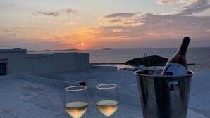Vista al atardecer desde una terraza en lo alto, con dos copas de vino blanco y una botella de champán en un cubo de metal.