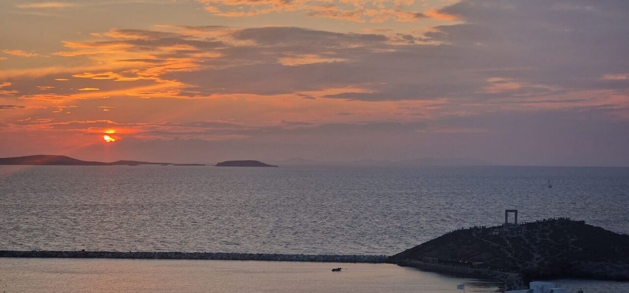 A coastal sunset with calm waters and a small island in the distance.