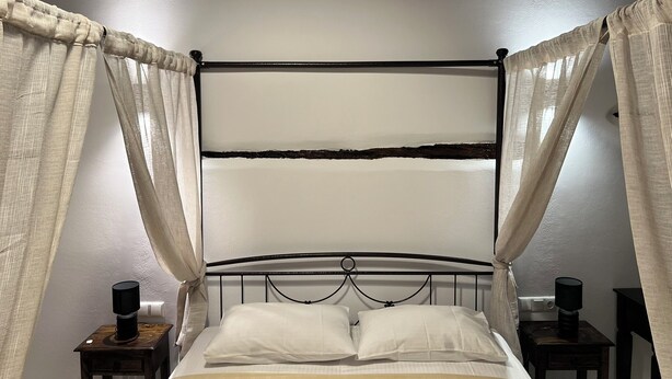 Una cama con estructura metálica, ropa de cama blanca y cabecera de madera. Hay dos mesitas de noche con lámparas.