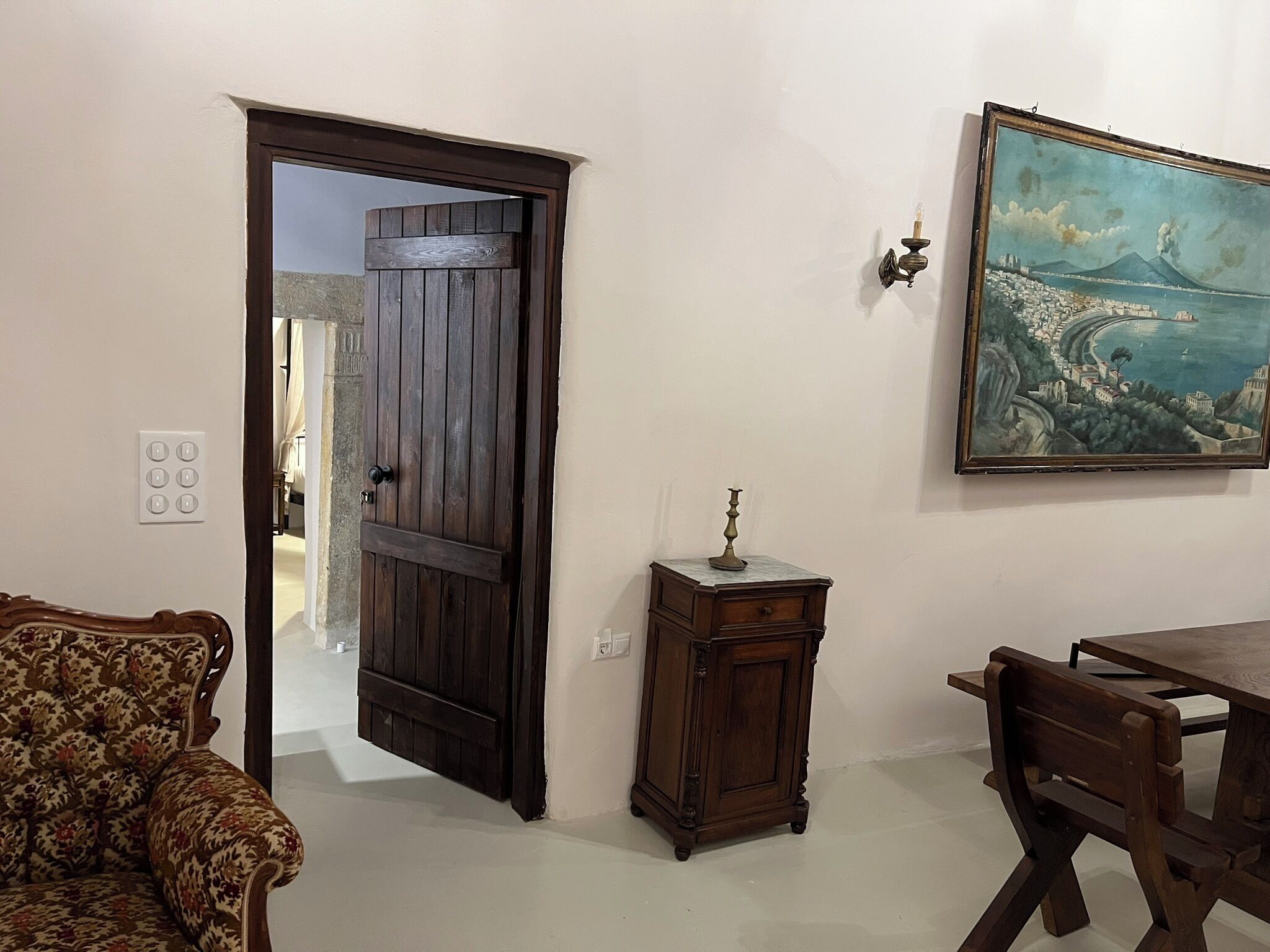 A room with a wooden door, a small cabinet, a dining table with chairs, and a wall-mounted painting.