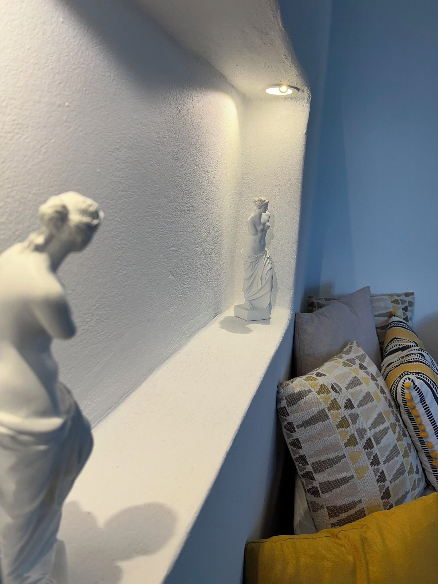 Une pièce avec un mur blanc et une étagère où sont exposées deux statues blanches.
