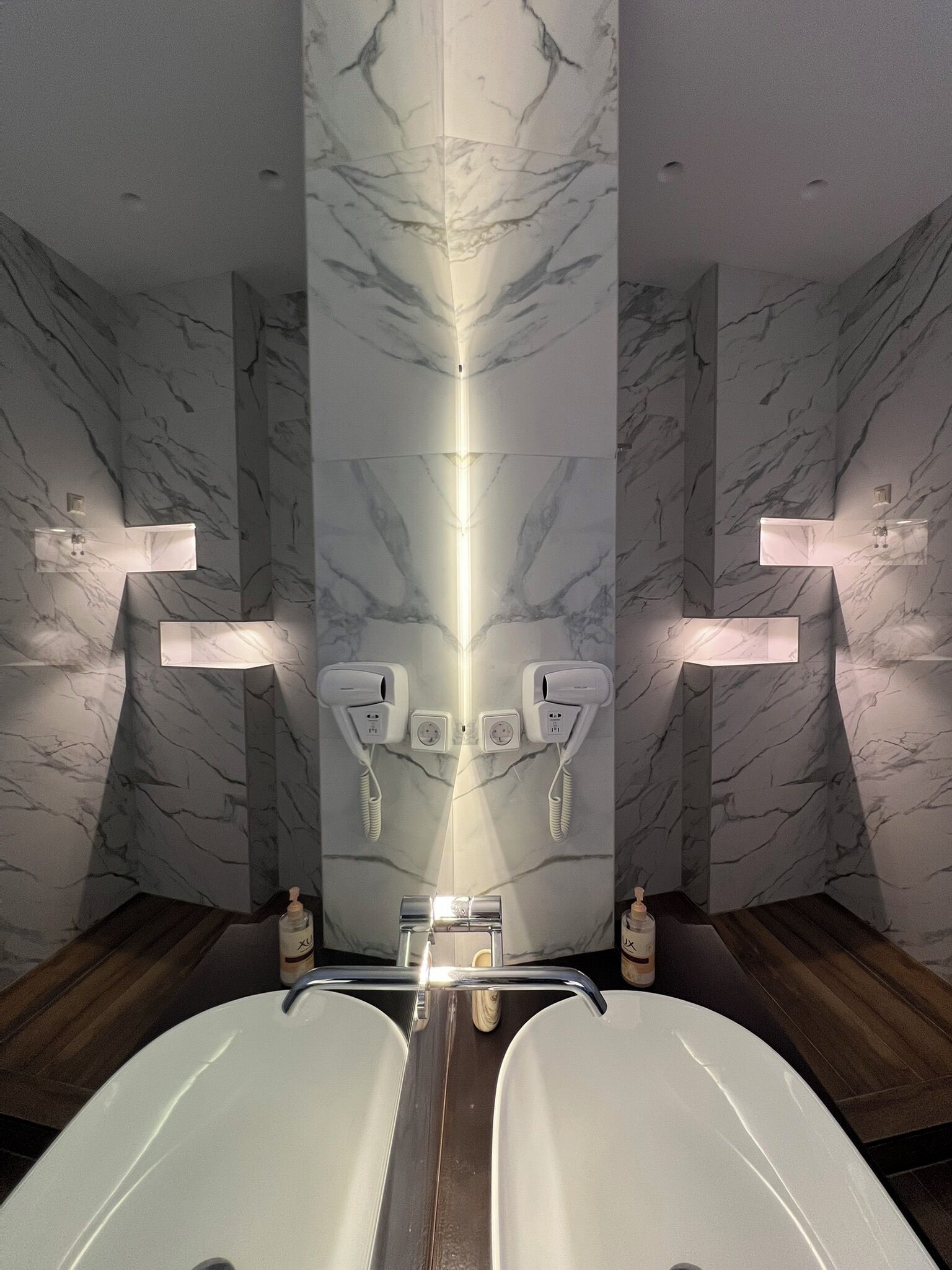 Ein modernes Badezimmer mit Marmorwänden, zwei Waschbecken und einer zentralen Leuchte.