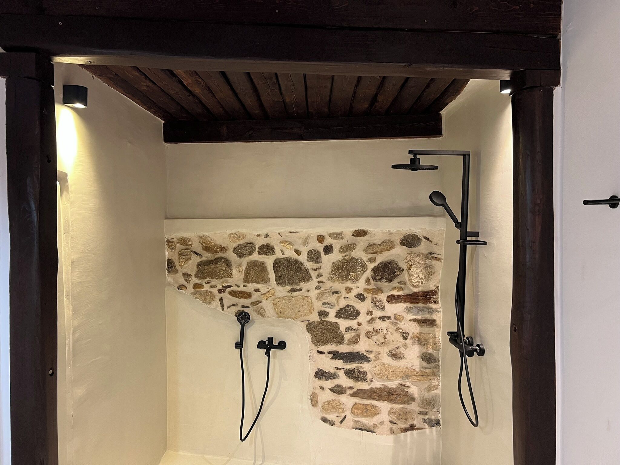 A shower with stone wall, wooden ceiling, and black fixtures.