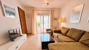 A modern living room with a flat-screen TV, a sofa, a coffee table, and a lamp. - 3 Bedroom Apartment on Golf Resort with Pool (Alhama de Murcia)