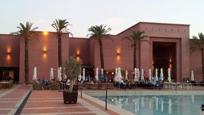 Un área junto a la piscina con una pileta grande, palmeras y mobiliario exterior.