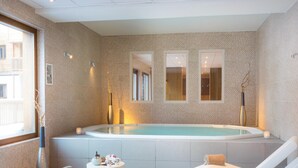 Egy modern wellness-szoba, amelyben egy nagy méretű fürdőkád, két pihenőfotel és egy kis asztal található, melyen minden szükséges felszerelés rendelkezésre áll.