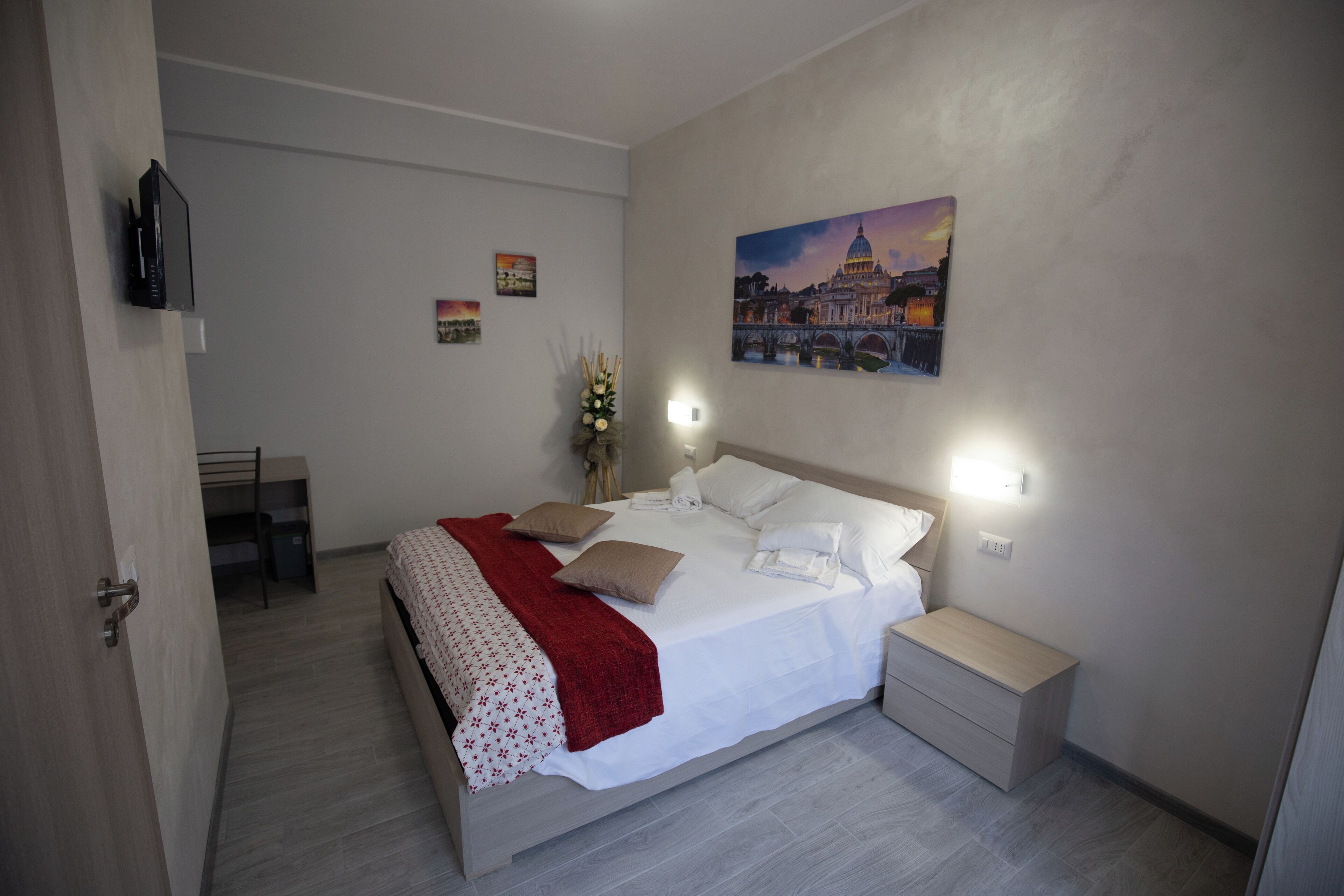 A neatly arranged bedroom with a bed, bedside tables, a nightstand, a TV, and a painting on the wall.