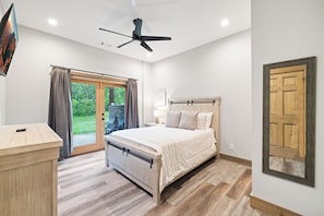 A bedroom with a bed, a wooden dresser, a ceiling fan, and a view of the outdoors through a sliding glass door.