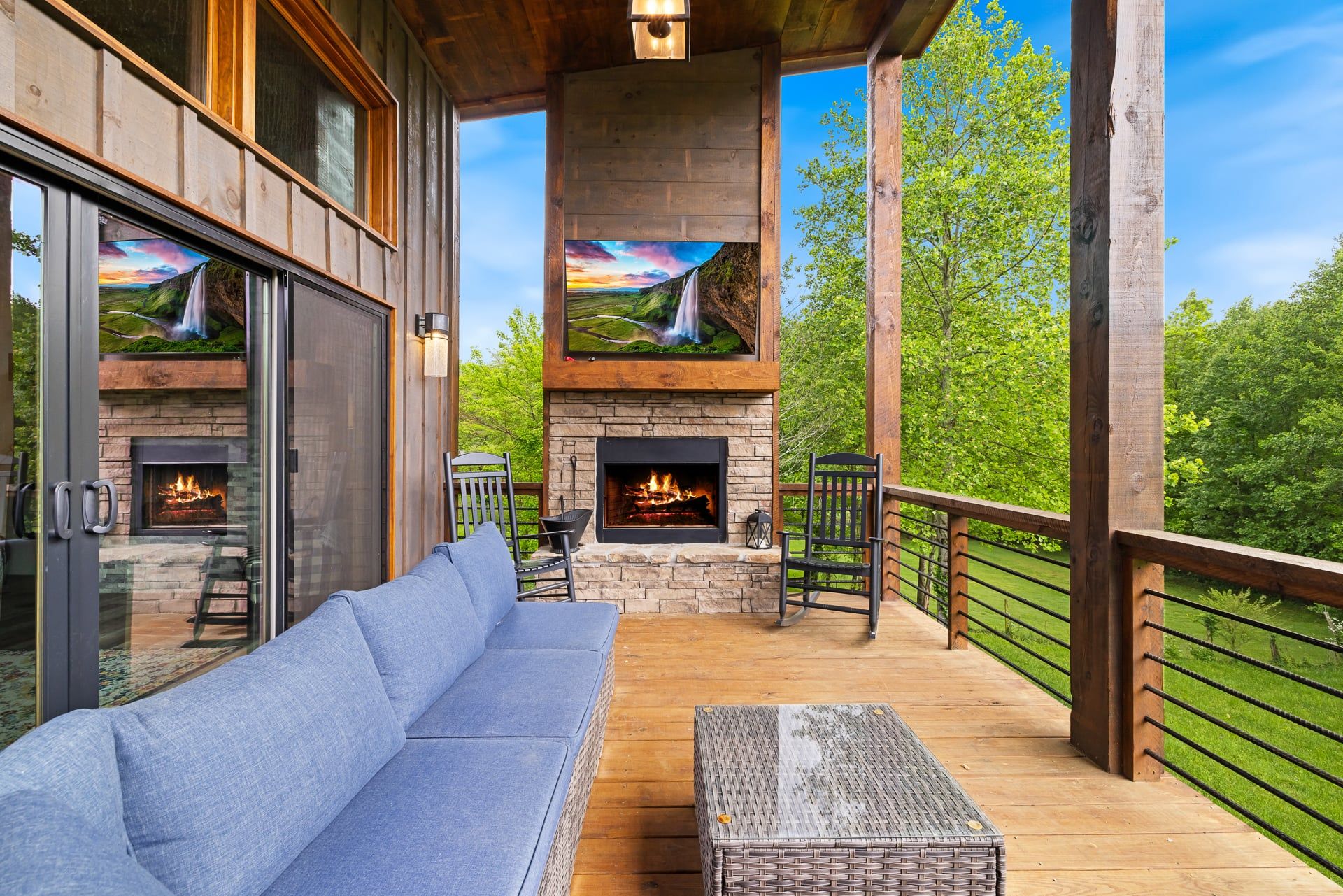 A wooden deck with a stone fireplace, a blue sofa, and a wicker ottoman.