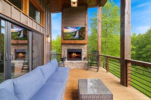 A wooden deck with a stone fireplace, a blue sofa, and a wicker ottoman.