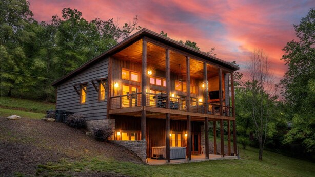Une cabane en rondins à deux étages, dotée d’un balcon et entourée d’arbres et d’une pelouse.