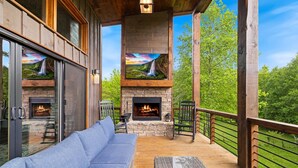 Une terrasse en bois avec une cheminée en pierre, un canapé bleu et un pouf en osier.